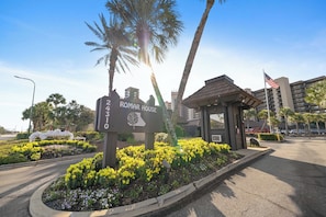 A hotel entrance with a sign, palm trees, and a building in the background.