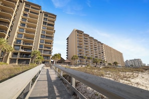 A beachfront hotel with multiple floors, balconies, and a wooden boardwalk leading to the beach.