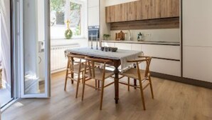 Une cuisine moderne avec des meubles en bois, une table à manger avec des chaises et une grande fenêtre qui laisse entrer la lumière naturelle.