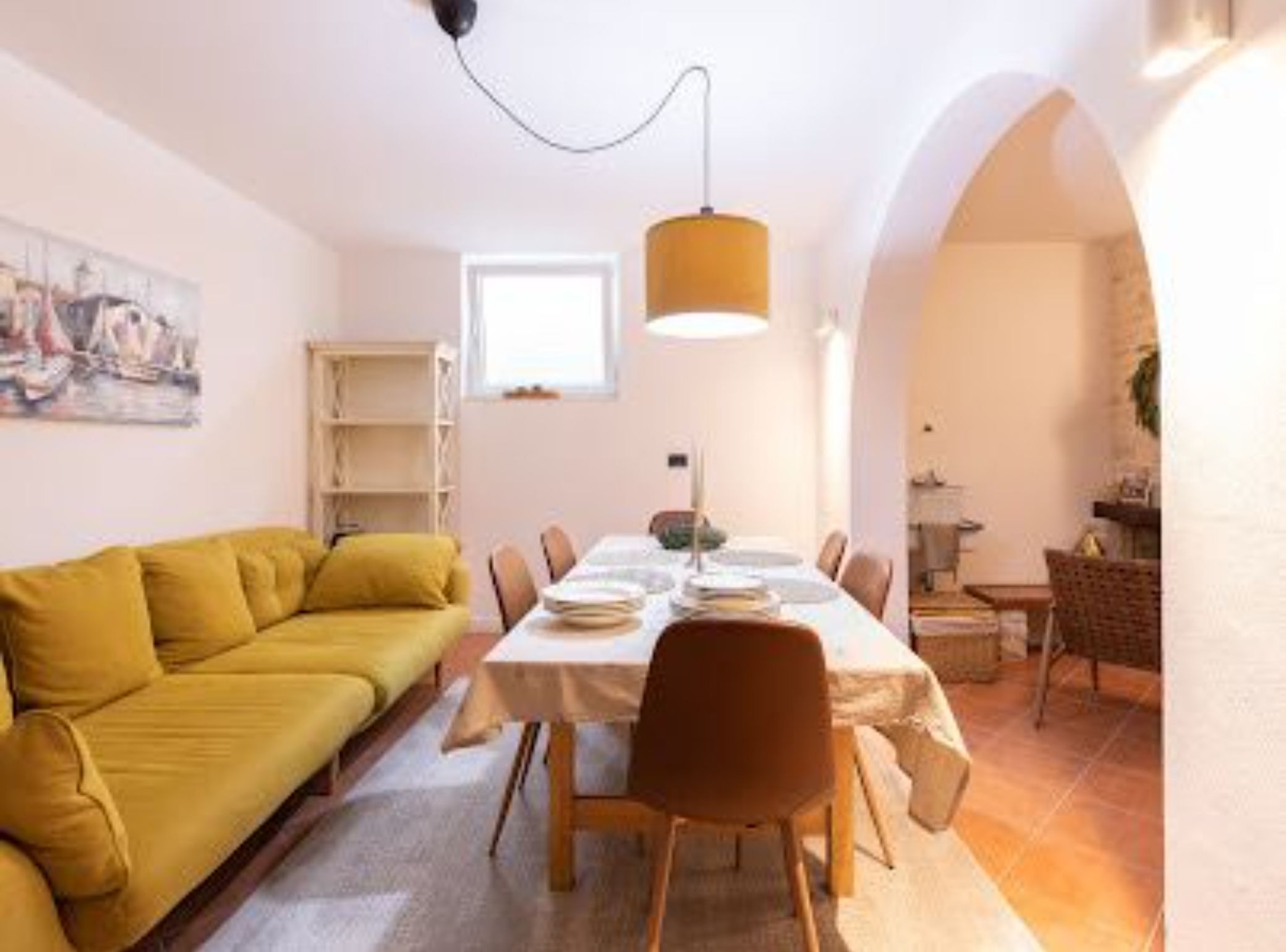 Un coin repas avec une table dressée pour quatre personnes, un canapé jaune et un luminaire suspendu.