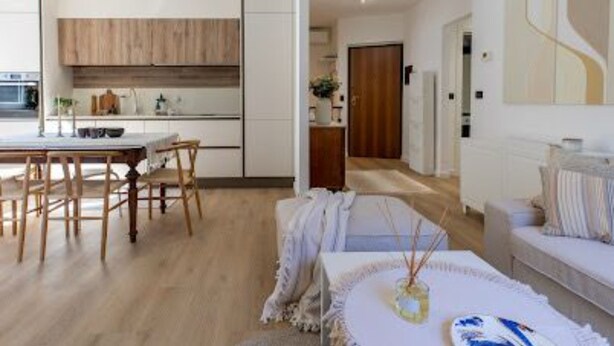Une cuisine moderne avec des meubles en bois, un coin repas avec une table et des chaises, et un salon avec un canapé et un vase décoratif.