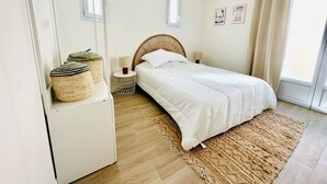 A bedroom with a bed, bedside lamps, a woven rug, and a window with curtains. - Maison jala (La Rochelle)