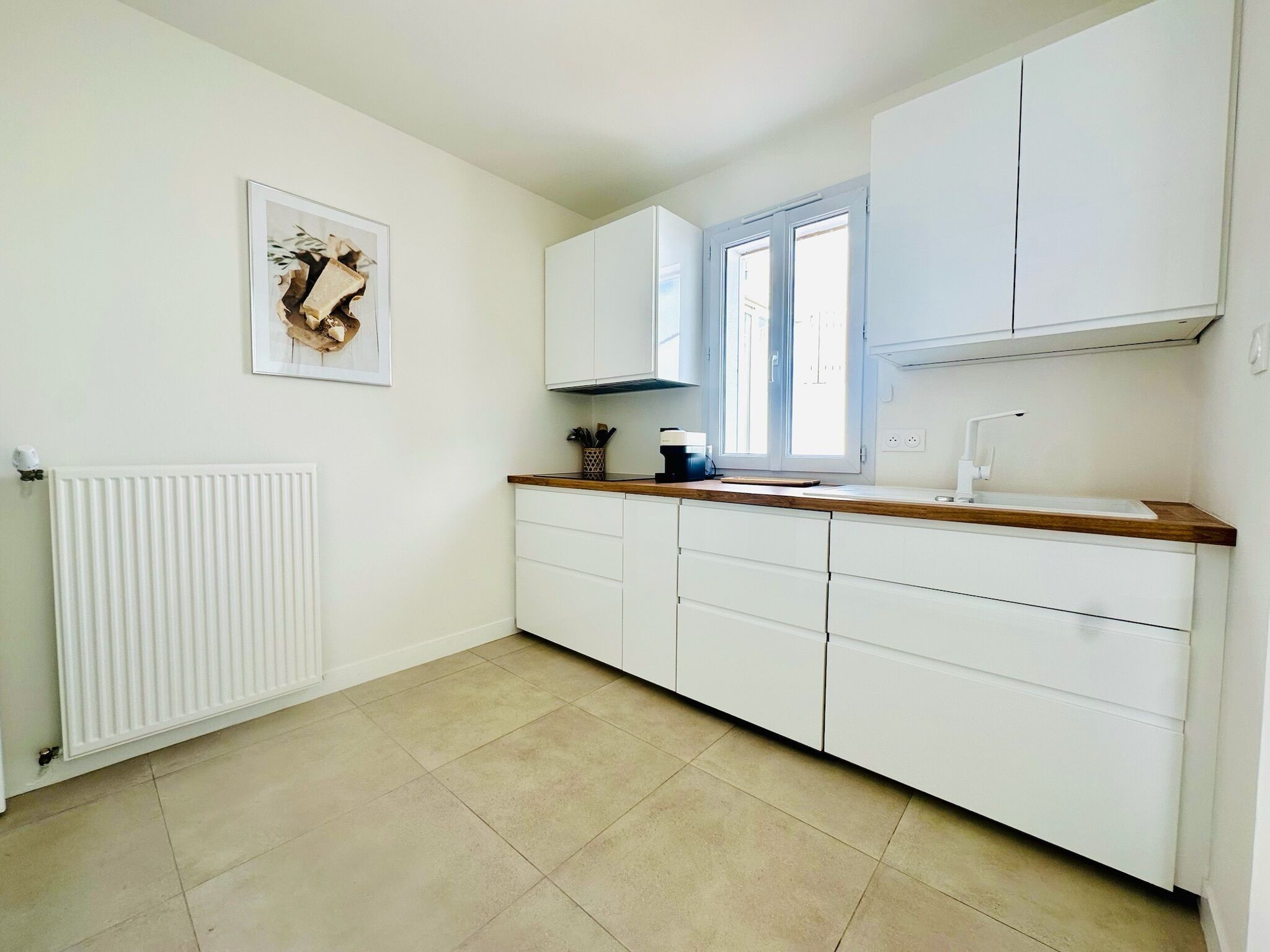 Una cocina con armarios blancos, encimera de madera, ventana y radiador.
