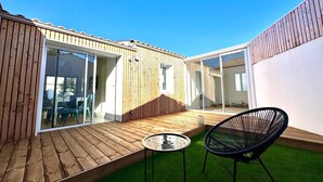 A modern outdoor patio with wooden decking, a small round table, and a black chair. - Maison jala (La Rochelle)