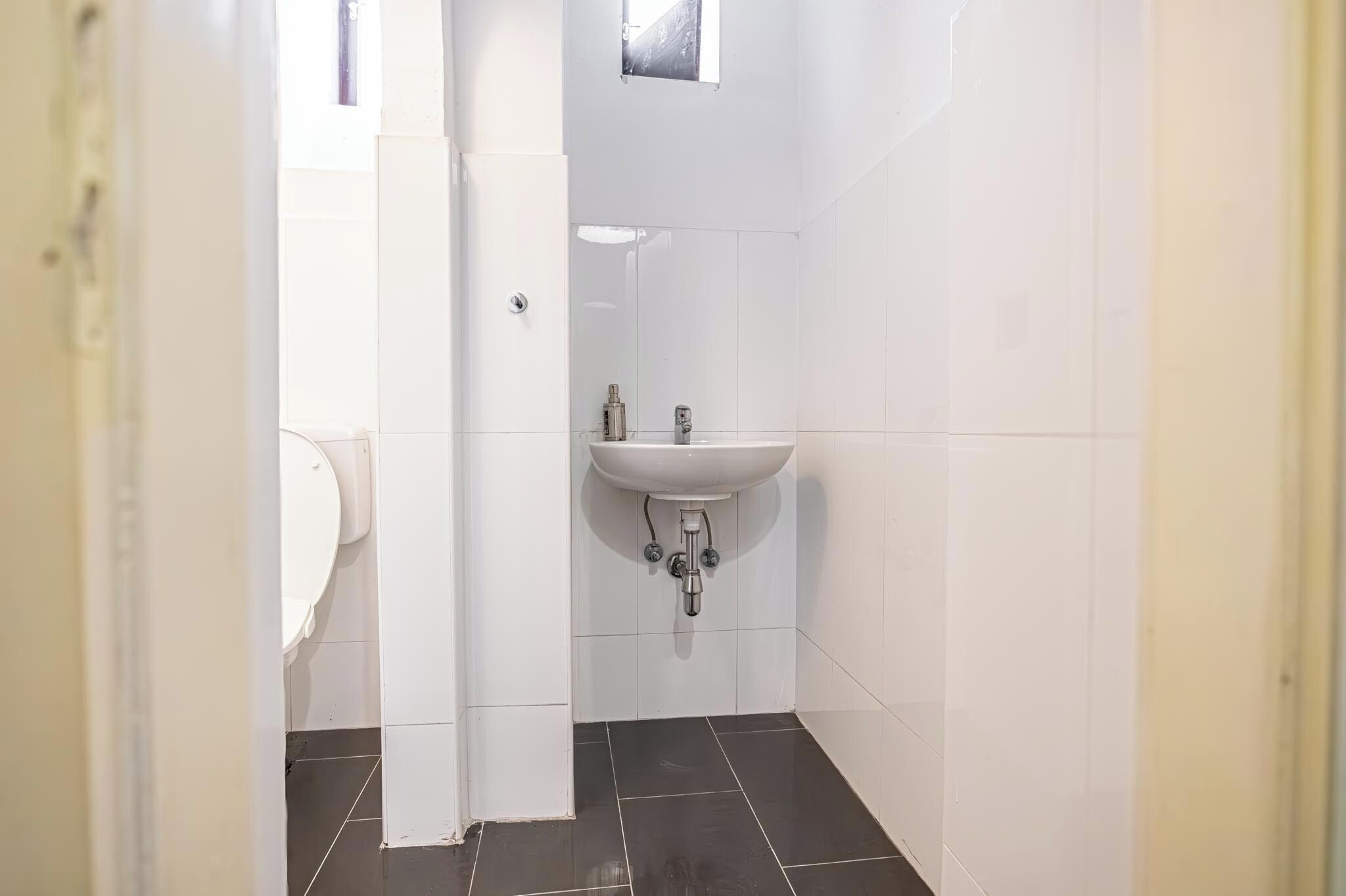 Une petite salle de bain propre, avec des carreaux blancs, un lavabo blanc et des toilettes.