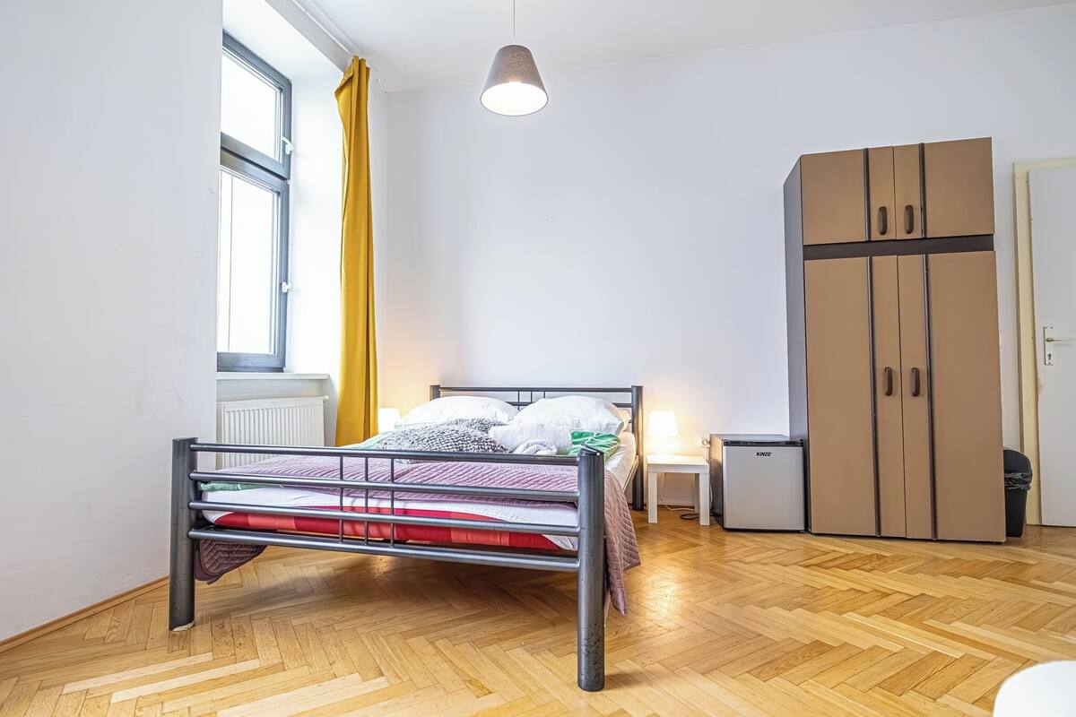 A bedroom with a metal bed frame, a wardrobe, a radiator, and a window with yellow curtains.