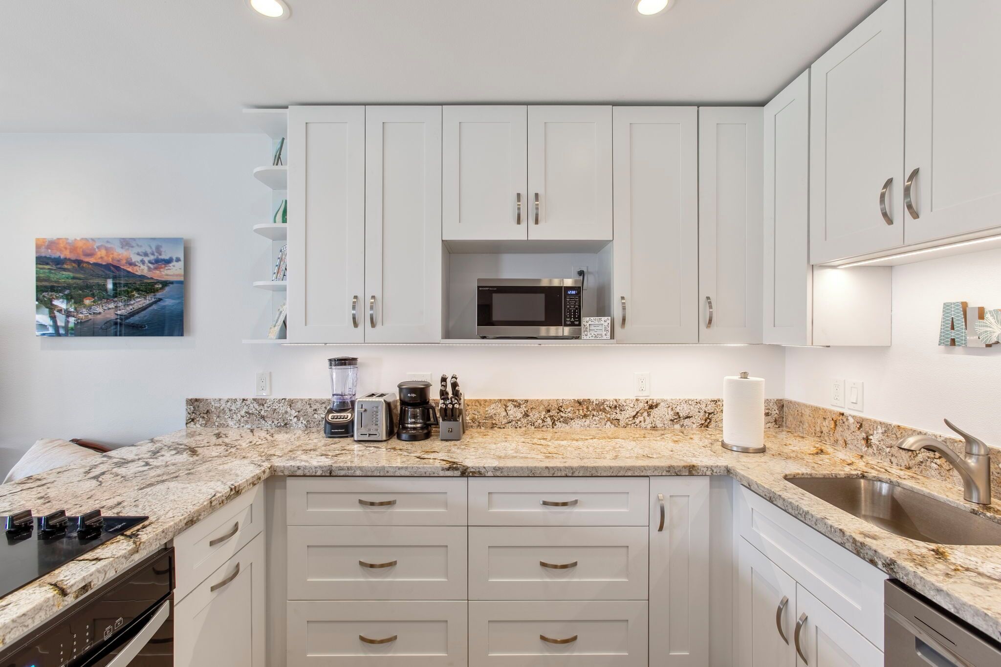 A modern kitchen with white cabinets, a granite countertop, a built-in microwave, and a coffee maker.
