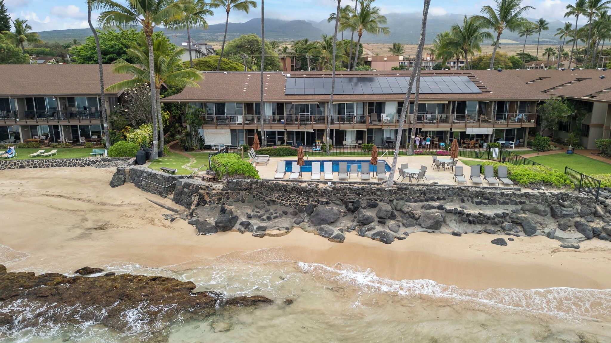 A beachfront hotel with a pool, outdoor seating, and solar panels.