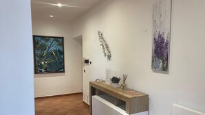 A hallway with a wooden reception desk, a framed painting of birds, and a wall-mounted plant.