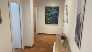 A hallway with a wooden reception desk, a painting of a tree, and a door leading to another room.
