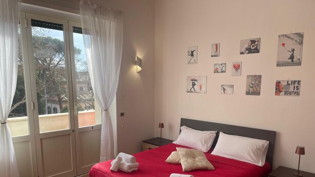 A bedroom with a bed, curtains, a nightstand, a wall with artwork, and a window.