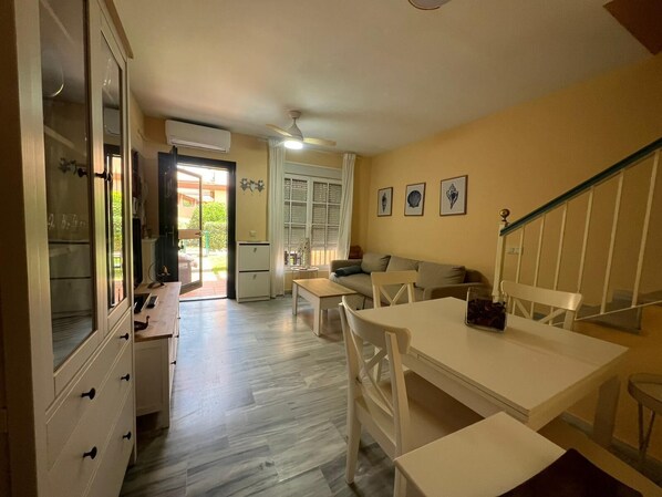 Amplia sala de estar con sofá, mesa de comedor y zona de cocina con refrigerador y armarios.