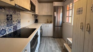 Een compacte keuken met lichte houten kastjes, een roestvrijstalen koelkast, een inbouwoven en een tegelpaneel met een patroon.
