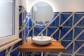 A bathroom with a white sink, a mirror, and blue patterned walls. - Maiori Suites (Maiori)