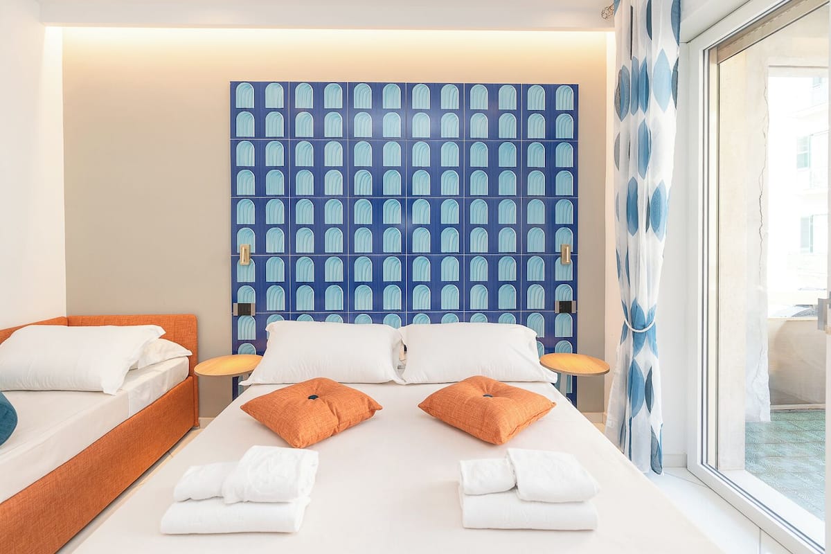 A hotel room with a bed, two pillows, a bedside table, and a wall with a blue pattern.
