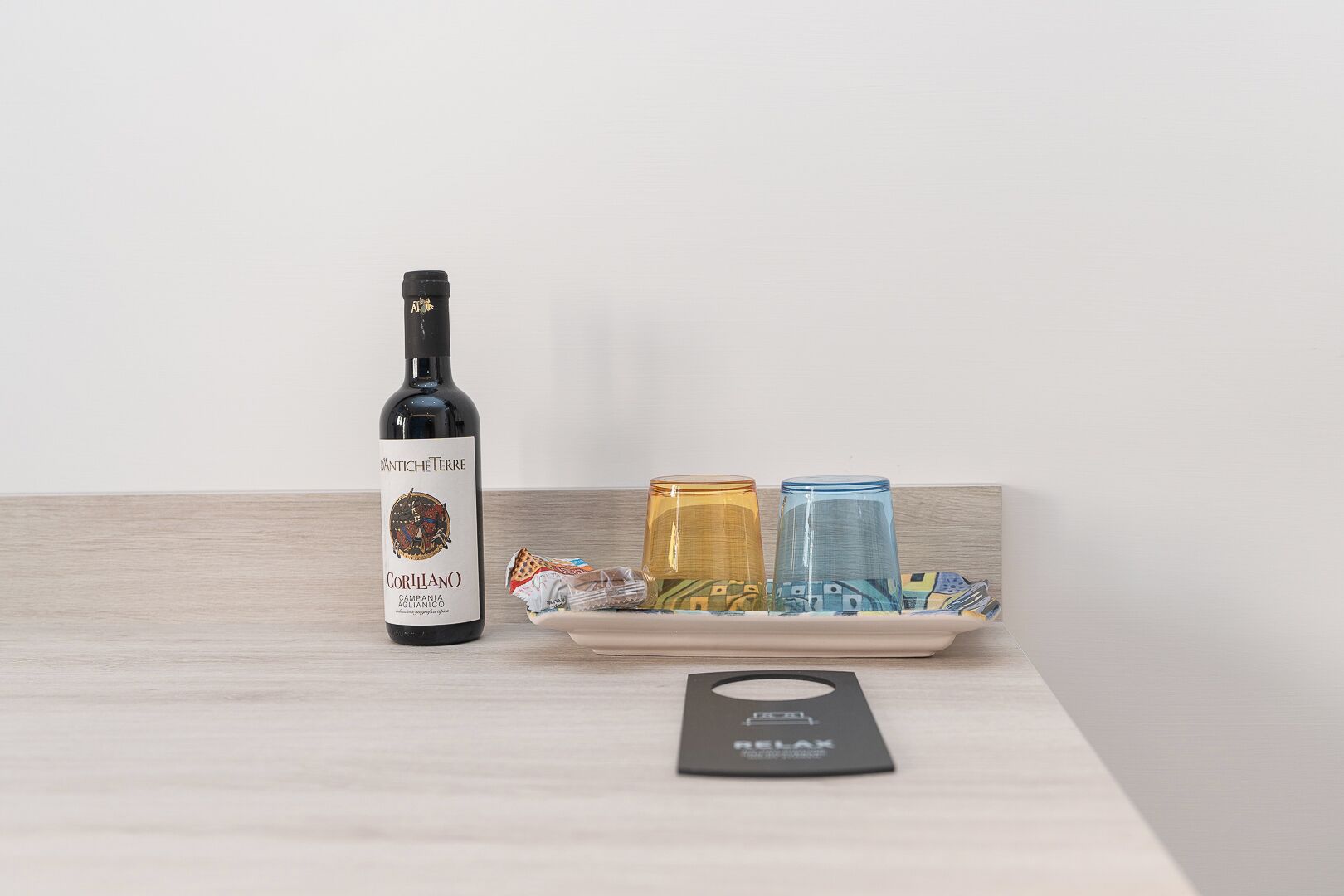 Una botella de vino Coriolino, dos copas coloridas y una colchoneta de relajación sobre una superficie de madera.
