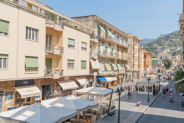 A bustling street with multi-story buildings, outdoor cafes, and a clear view of the surrounding hillside. - Maiori Suites (Maiori)
