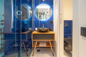 A modern bathroom with a wooden vanity, a large mirror, and a blue tiled wall. - Maiori Suites (Maiori)