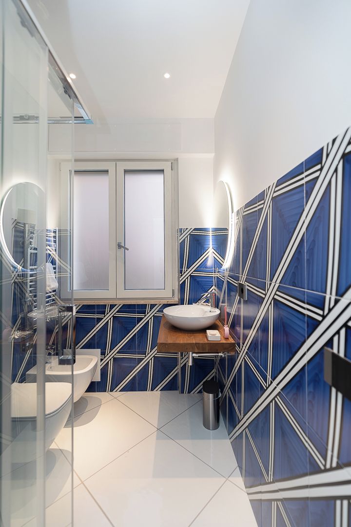 Un baño moderno con un lavamanos blanco, un espejo y una pared con estampado geométrico azul.