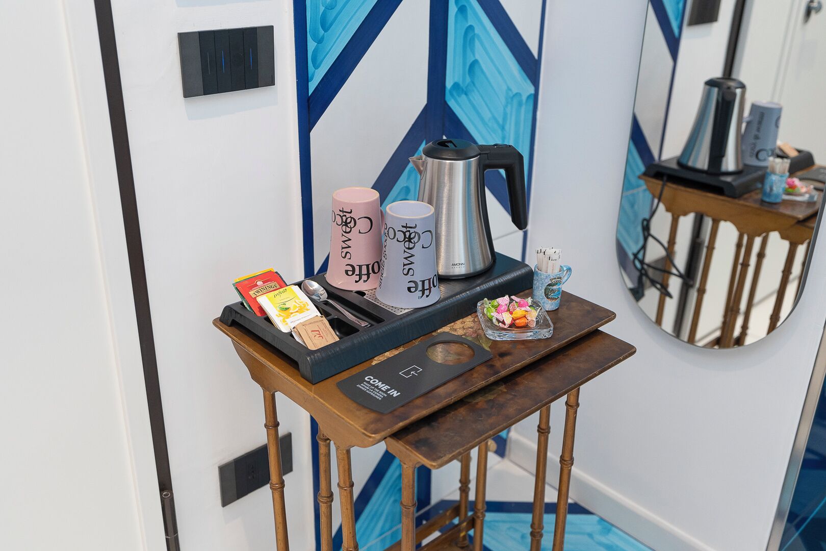 A small wooden table with a coffee maker, a tea set, and a tray with snacks.