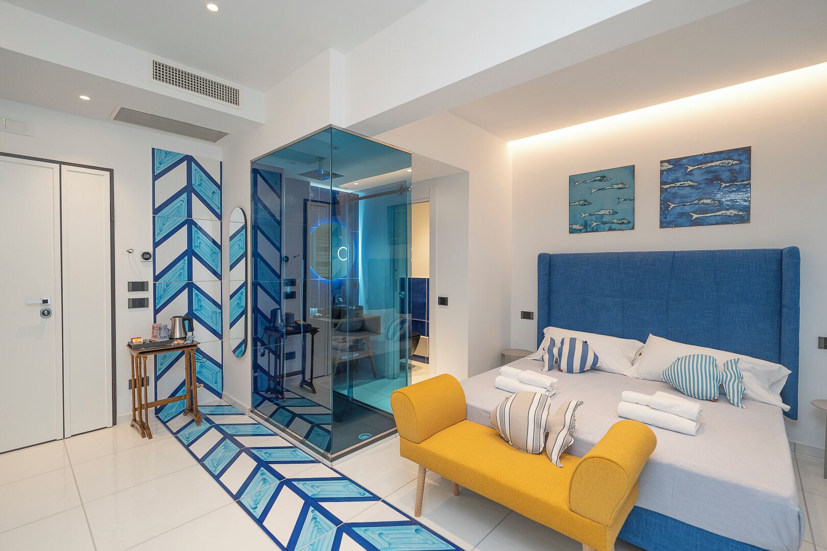 Een moderne slaapkamer met een groot bed, een gele fauteuil en een glazen scheiding.