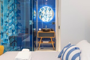 A modern bathroom with a geometric tile backsplash, a round mirror, and a wooden vanity with a bowl sink. - Maiori Suites (Maiori)