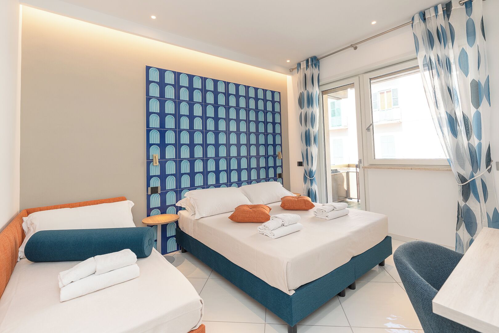 Une chambre d’hôtel moderne avec un grand lit, deux petits lits, une salle de bain et une vue sur la ville.