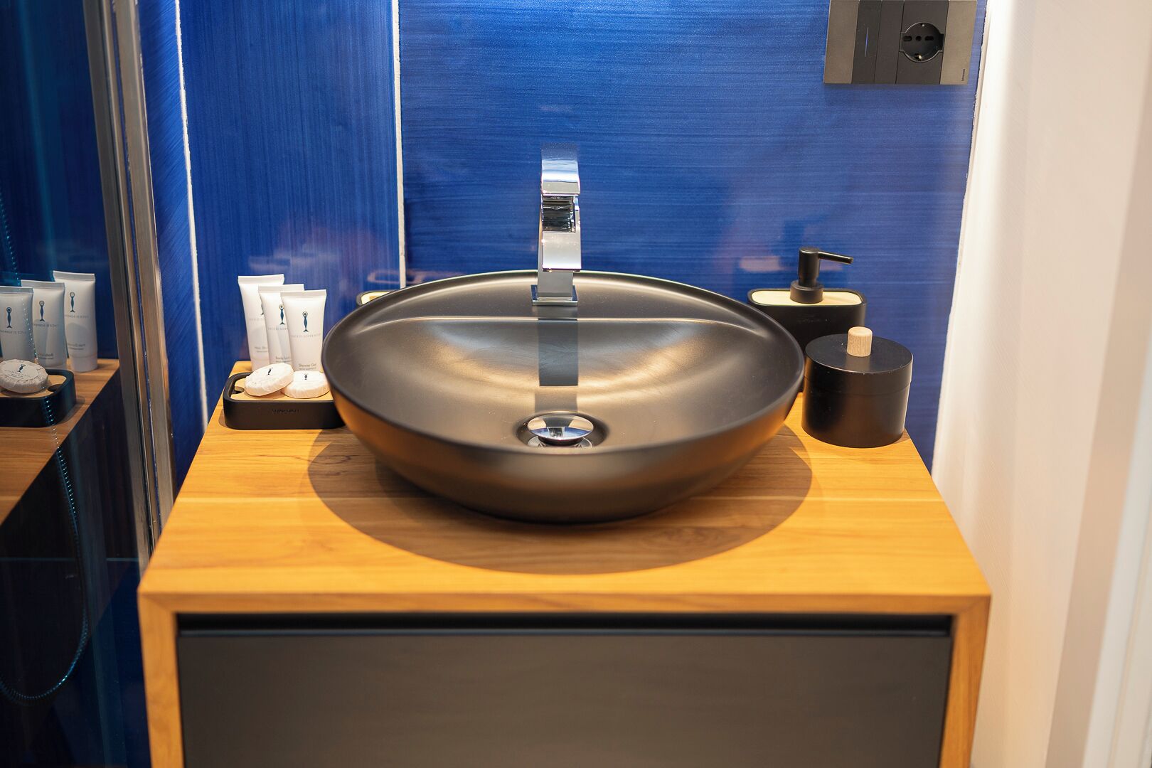 A modern bathroom with a large, round vessel sink, a mirror, and a shelf with toiletries.