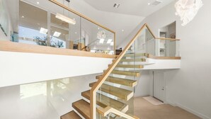 A modern staircase with glass railings and wooden steps, leading to a second-floor area with a view of the outdoors.