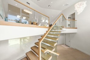 A modern staircase with glass railings and wooden steps, leading to a second-floor area with a view of the outdoors.