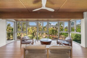 Une pièce spacieuse avec de grandes fenêtres, un ventilateur de plafond et un plancher en bois.