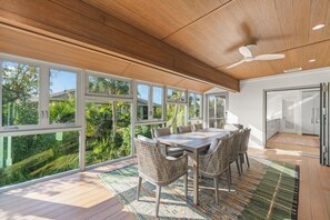 Un espace repas comprenant une table et des chaises, de grandes fenêtres et un ventilateur de plafond.