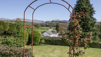 Un jardín con un arco de metal, abundante vegetación y una casa al fondo.