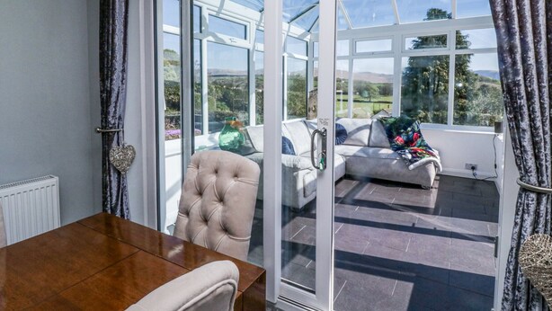 Une véranda avec une porte en verre, une table en bois et un fauteuil rembourré.