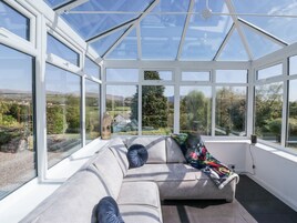A conservatory with a grey sofa, a colorful throw blanket, and an owl sculpture.