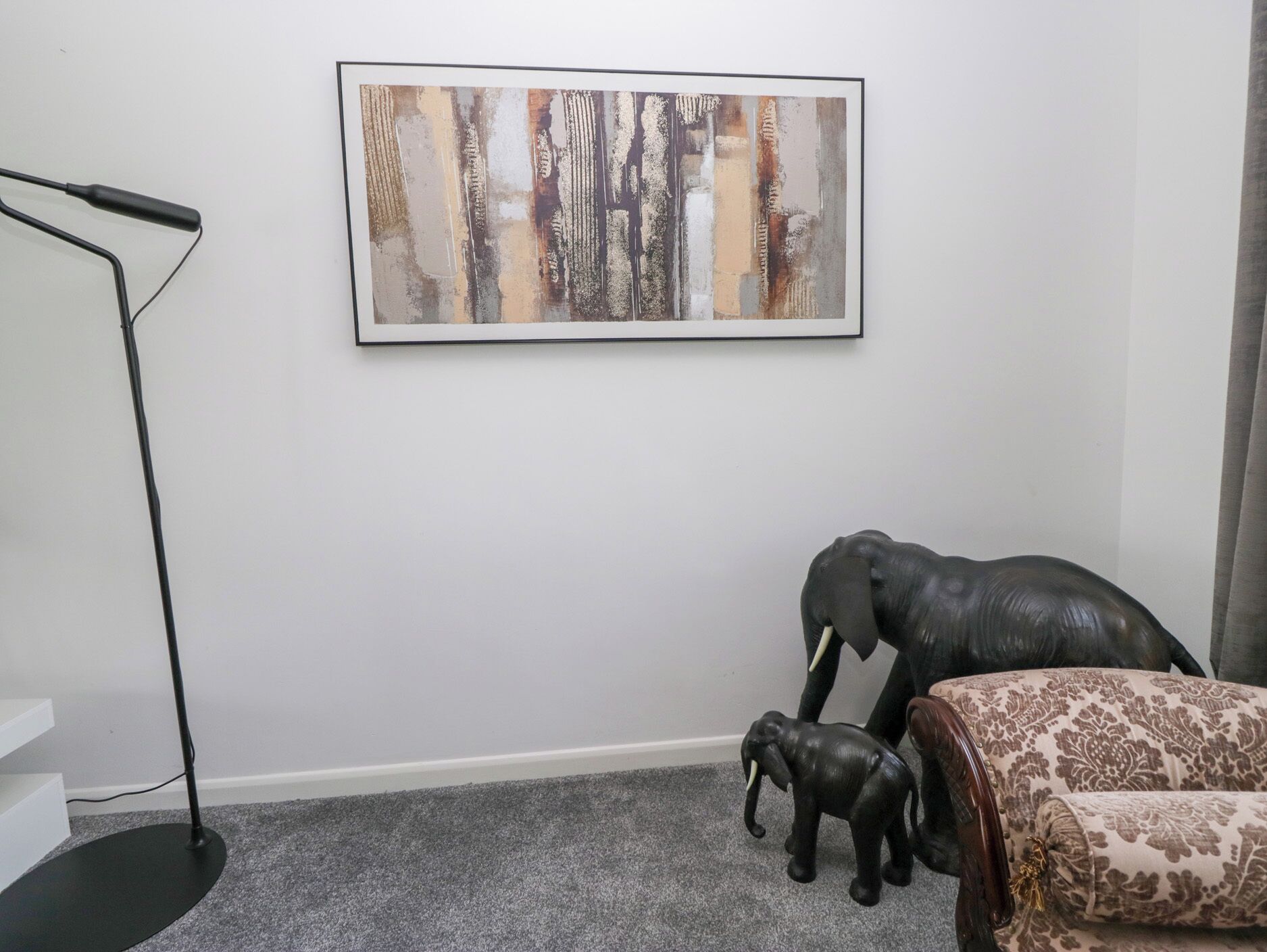 Une pièce décorée avec un tableau abstrait encadré, un lampadaire et un canapé agrémenté de coussins à motifs.