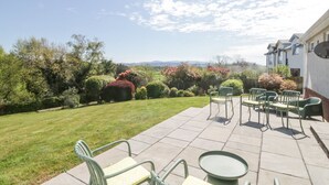 Une terrasse avec des meubles d’extérieur, une pelouse bien entretenue et une vue sur un quartier résidentiel avec des maisons et des arbres.