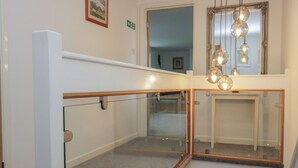 Un intérieur moderne avec une balustrade en verre, un miroir et un luminaire suspendu.