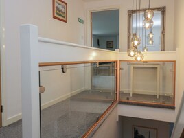 A modern interior with a glass railing, a mirror, and a hanging light fixture.