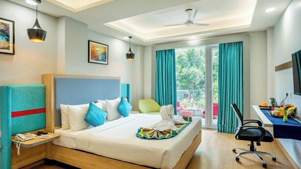 Habitación de hotel con cama, escritorio, silla, teléfono y ventana con cortinas.