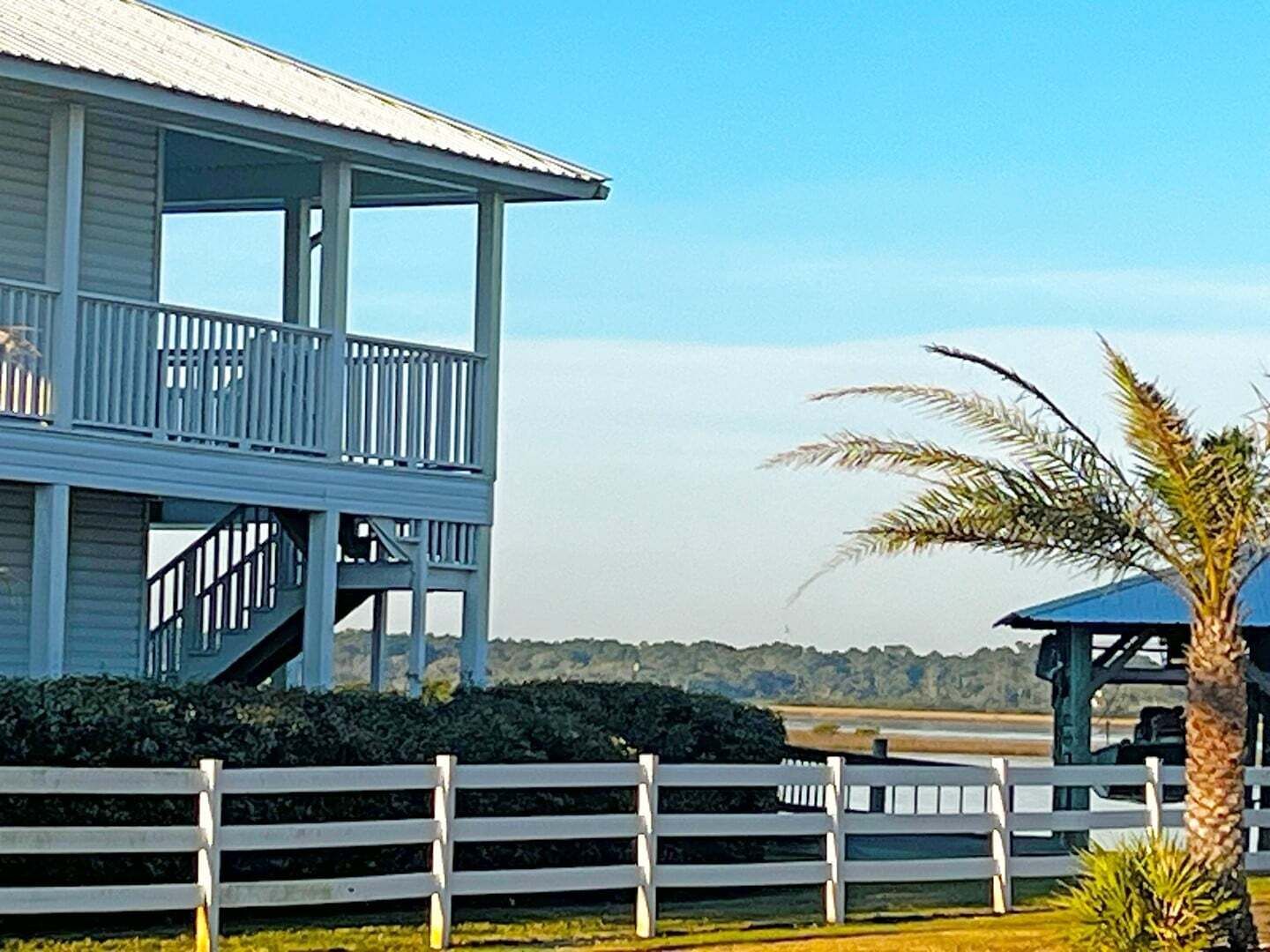 A two-story building with a balcony, a fenced area, and a palm tree.