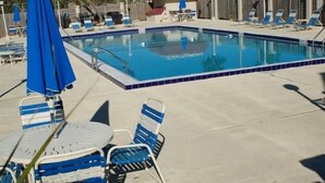 Ein Swimmingpool mit blau gefliesten Rändern, umgeben von Liegestühlen und Sonnenschirmen.