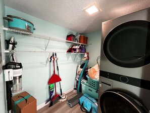 Een wasserette met een wasmachine, een droogrek en planken met schoonmaakmiddelen.