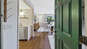 Un pasillo con una puerta verde, una zona de cocina con salpicadero de azulejos y un área de descanso con vistas al exterior.