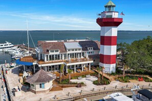 A lighthouse with a red and white striped tower, a white building with a wooden deck, and a marina with boats.