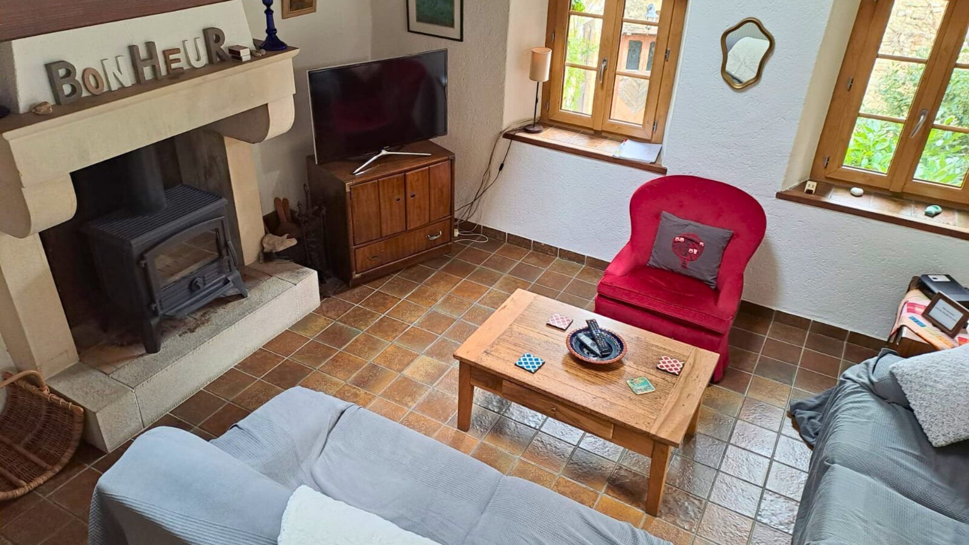 Una sala de estar con chimenea, televisor, un sillón rojo y un sofá.