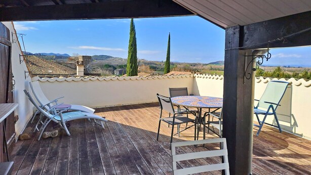 A wooden deck with a table and chairs, overlooking a scenic landscape with hills and trees.