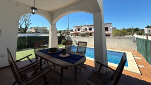 A covered patio with a pool, wooden furniture, and a view of surrounding buildings. - Villa with private Pool/Aircon/Wi-Fi - Villa Montgrí (L'Escala)
