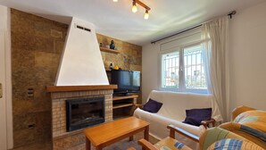 A living room with a fireplace, a sofa, a TV, and a window with curtains. - Villa with private Pool/Aircon/Wi-Fi - Villa Montgrí (L'Escala)