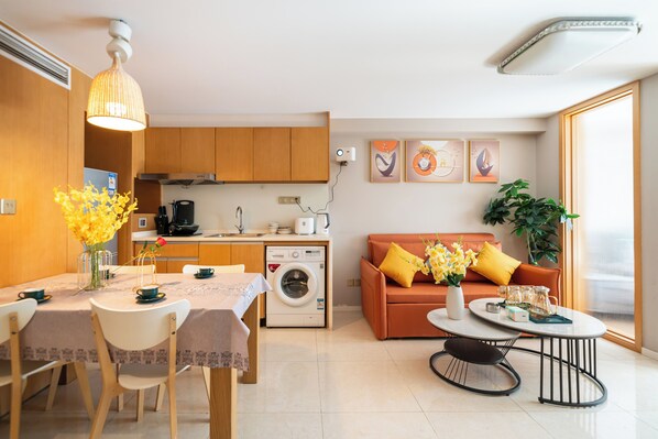 Un espace de vie compact comprenant un coin repas, une kitchenette et un canapé avec des coussins jaunes.